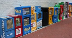 Eine Reihe von 14 bunten Zeitungsautomaten, wie sie oft in Großbritannien oder Amerika zu finden sind.